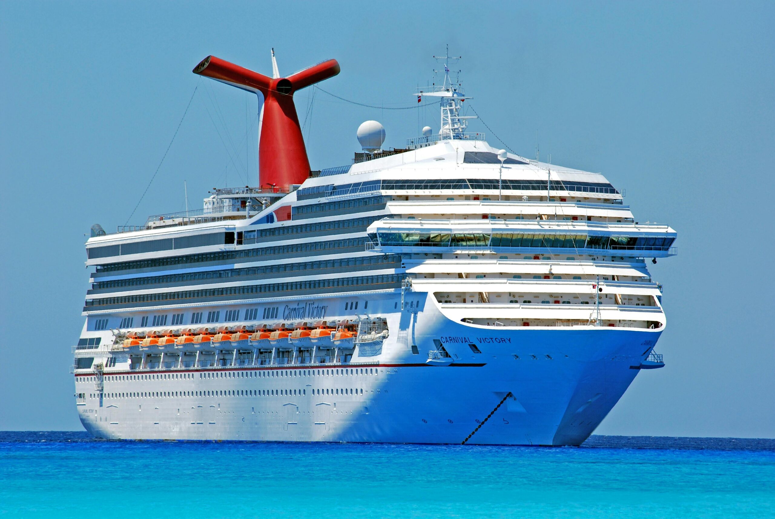 A large cruise ship gliding through clear blue ocean waters on a sunny day.